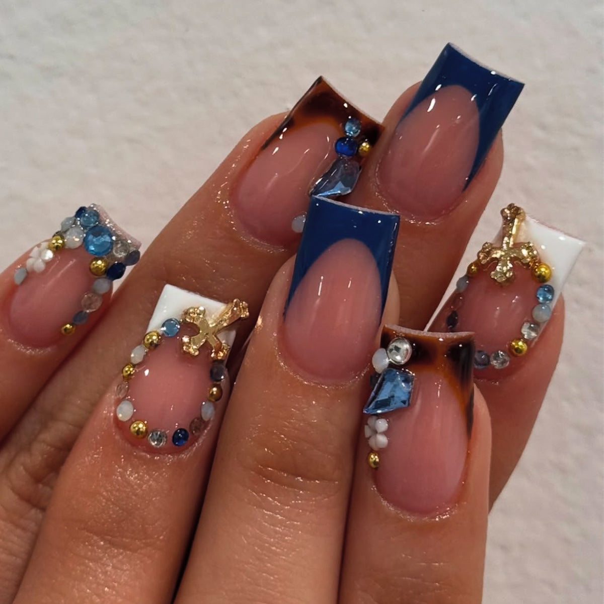 Model wearing navy blue rhinestone French square press-on nails with sparkling cross details