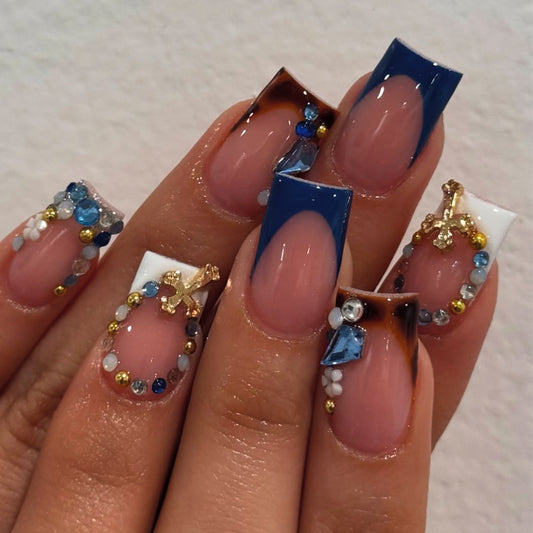Model wearing navy blue rhinestone French square press-on nails with sparkling cross details